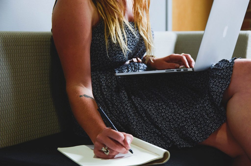 person writing on a notebook beside macbook